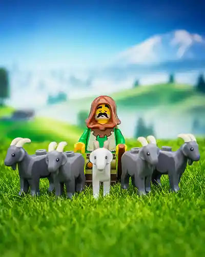 A LEGO shepherd minifigure stands solemnly in a grassy field, surrounded by six goats with a scenic mountain backdrop.
