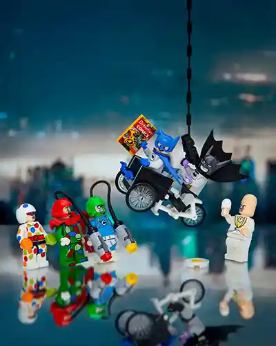 LEGO Batman and Bat-Mite swing away on a bike holding a Detective Comics cover, escaping from colorful villains including Polka-Dot Man and Egghead, with a city backdrop and egg on the ground.