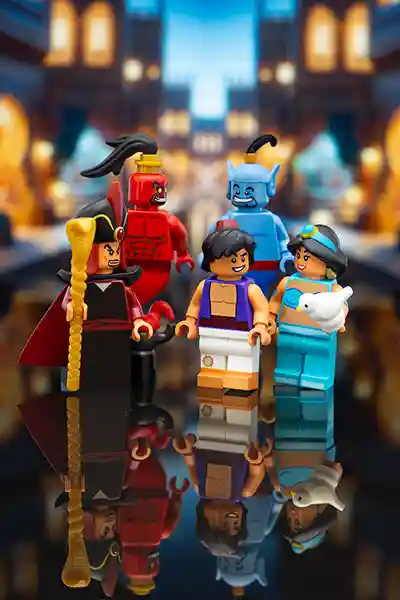 LEGO minifigures of Aladdin, Jasmine holding a white bird, Genie, Jafar, and red Genie Jafar stand together in a magical city setting with a warm, glowing background.
