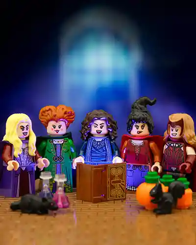 LEGO minifigures of Wanda Maximoff and Agatha Harkness from the MCU stand alongside the Sanderson Sisters from Hocus Pocus, gathered around a magical spellbook with potions, pumpkins, and spooky creatures. A glowing window backdrop hints at witchy mischief in this Disney crossover.
