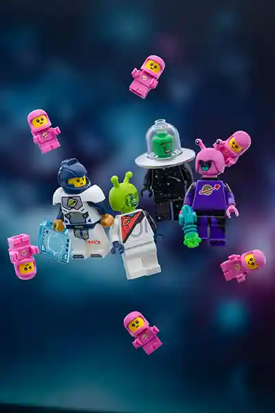 A cheerful group of LEGO space minifigures float in zero gravity, including classic spacemen and colorful aliens surrounded by a dozen adorable pink space babies, all set against a dreamy galactic backdrop.