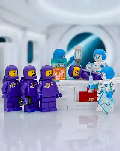 A group of purple LEGO astronauts anxiously watch as one of their crew members receives a vaccination from futuristic blue-haired medics in a white sci-fi medical bay.