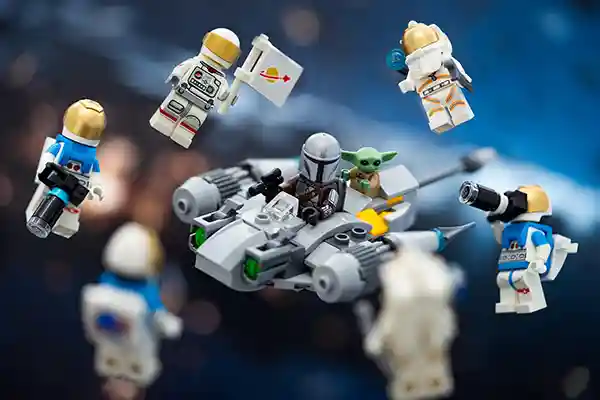 LEGO Mandalorian and Grogu fly an N-1 Starfighter through space, surrounded by Classic Space astronauts in gold-domed helmets capturing the moment with cameras, tools, and a flag.