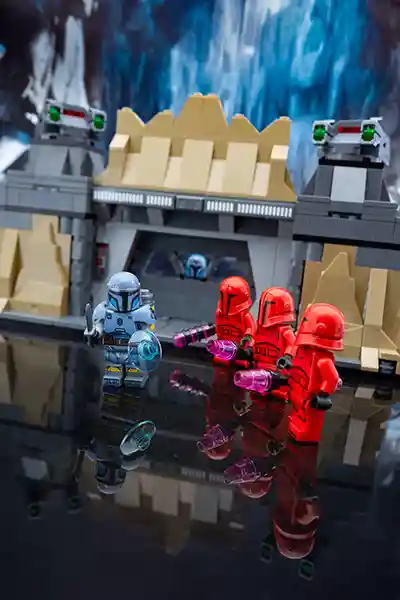 A lone LEGO Mandalorian warrior Paz Vizsla confronts three Praetorian Guards outside a fortress gate, while another Mandalorian watches from within.