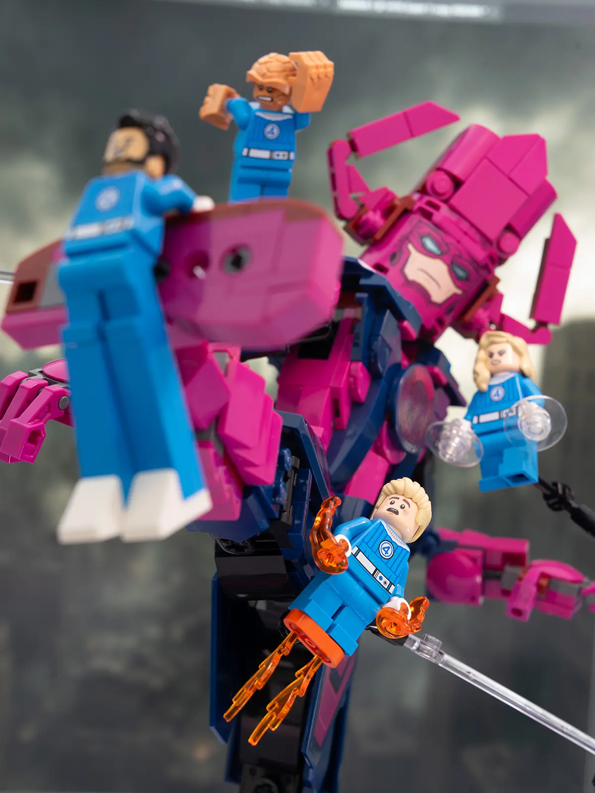 LEGO Fantastic Four minifigures face off against a towering Galactus figure. Mr. Fantastic, Invisible Woman, Human Torch, and The Thing are suspended mid-action with visible Support bars, set against a cloudy city backdrop.