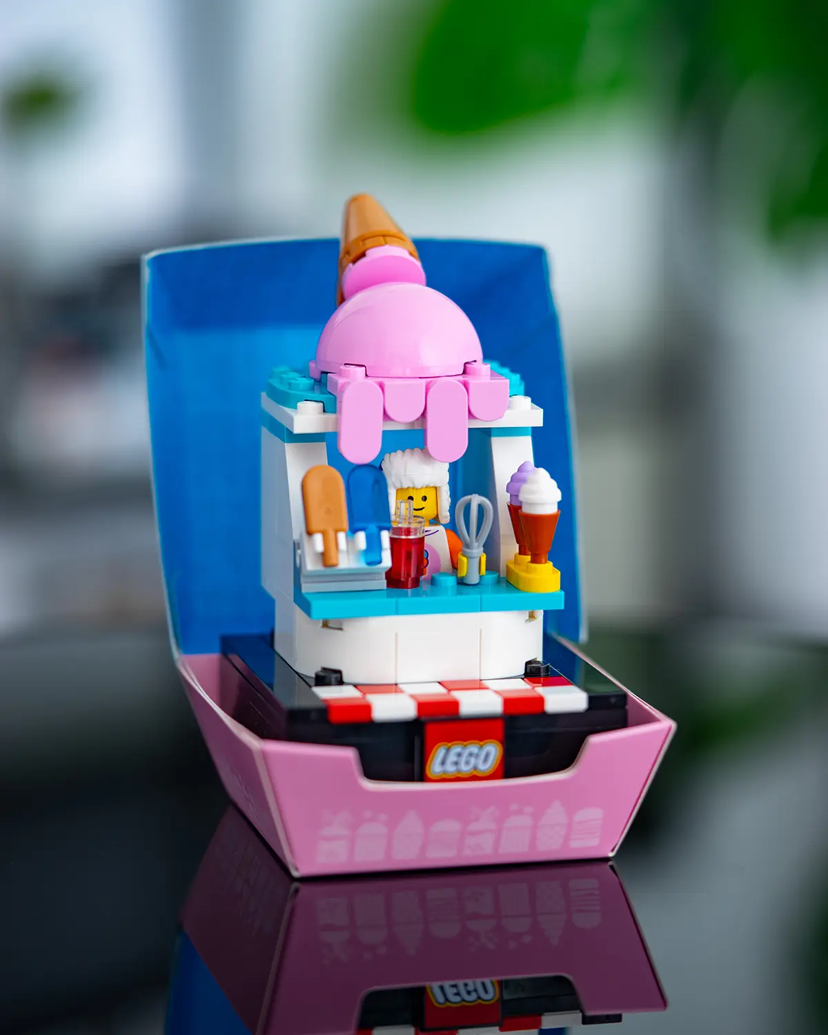 LEGO ice cream stand build with a giant pink ice cream cone on top, featuring a minifigure server and various frozen treats on display.