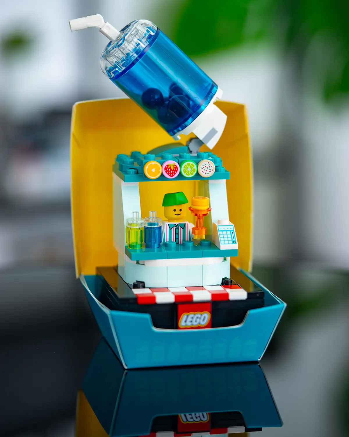 LEGO smoothie or juice bar stand with a large transparent blue drink cup on top, a minifigure vendor, and colorful drink bottles on the counter.