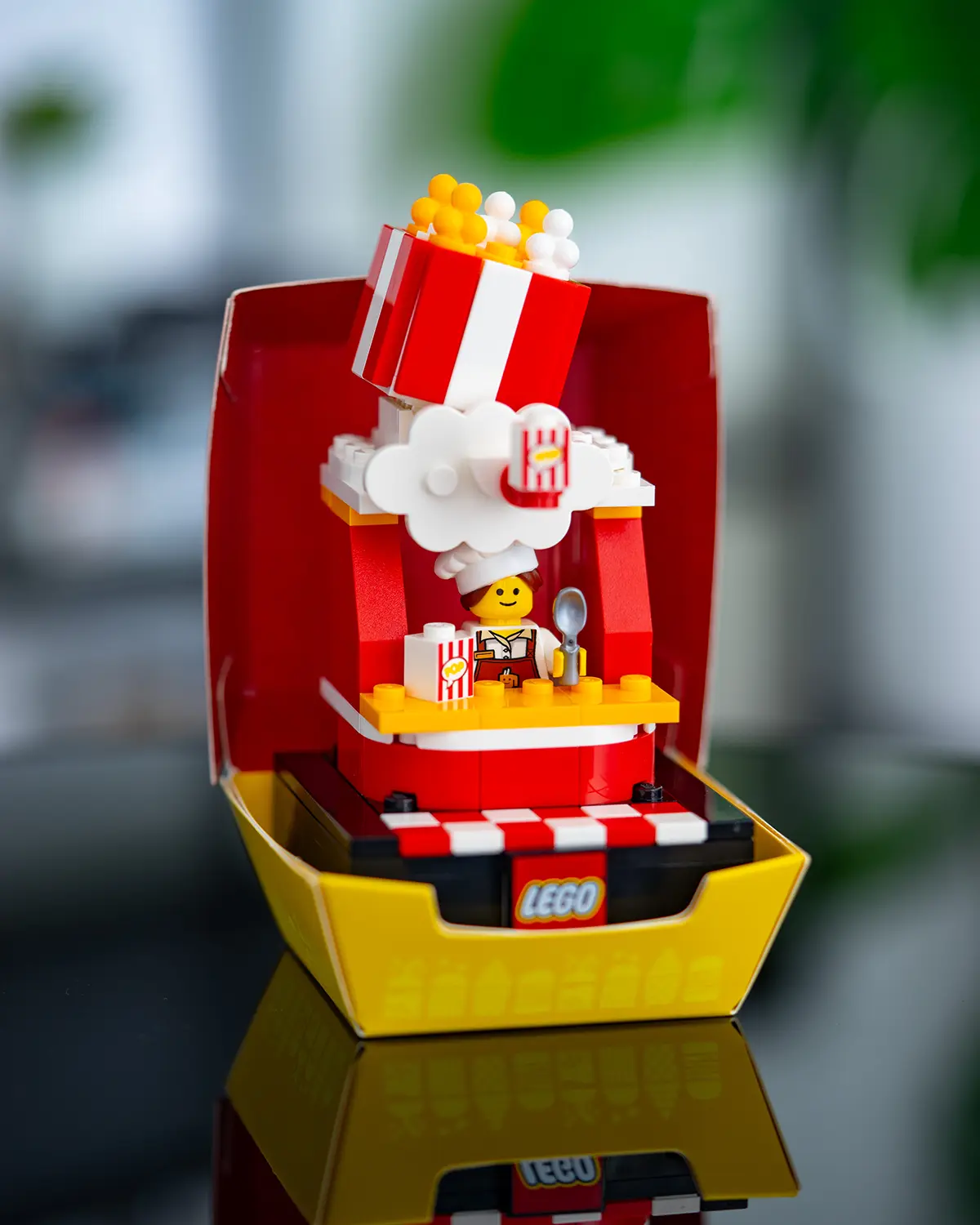 LEGO popcorn cart featuring a giant striped popcorn box overflowing with kernels, with a cheerful minifigure vendor holding a spoon and popcorn tub.