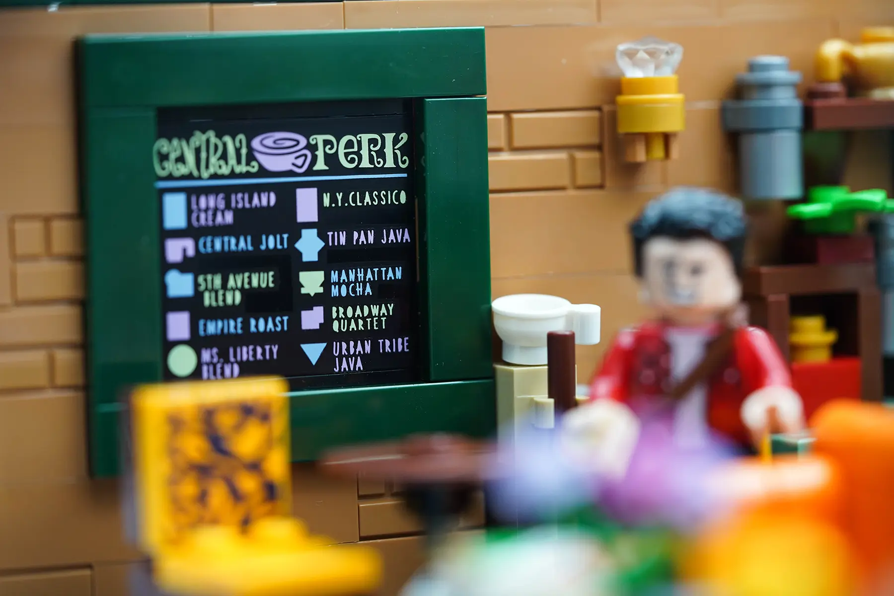 Close-up of the LEGO Central Perk menu board showing playful coffee names with a blurred minifigure of Joey in front.