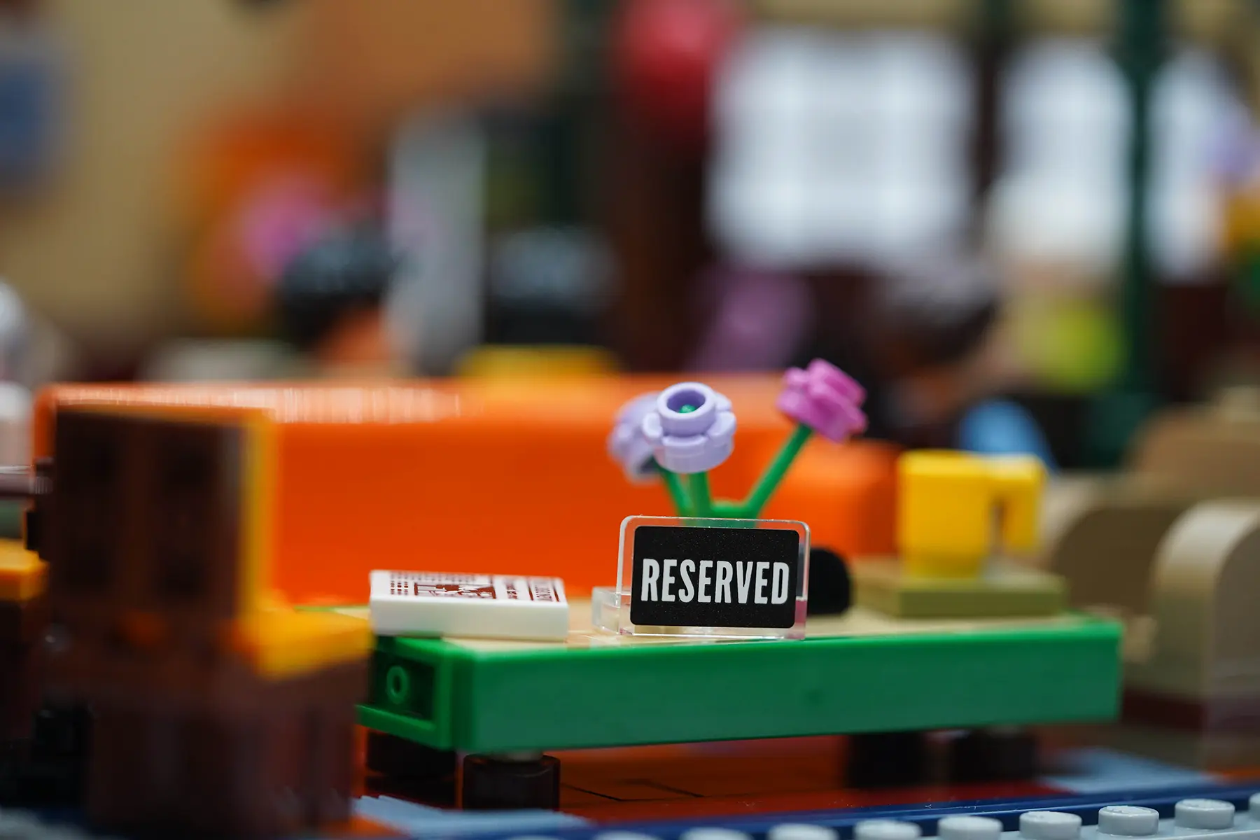 A LEGO table with flowers and a “Reserved” sign in front of the Friends' orange couch and chairs at Central Perk.