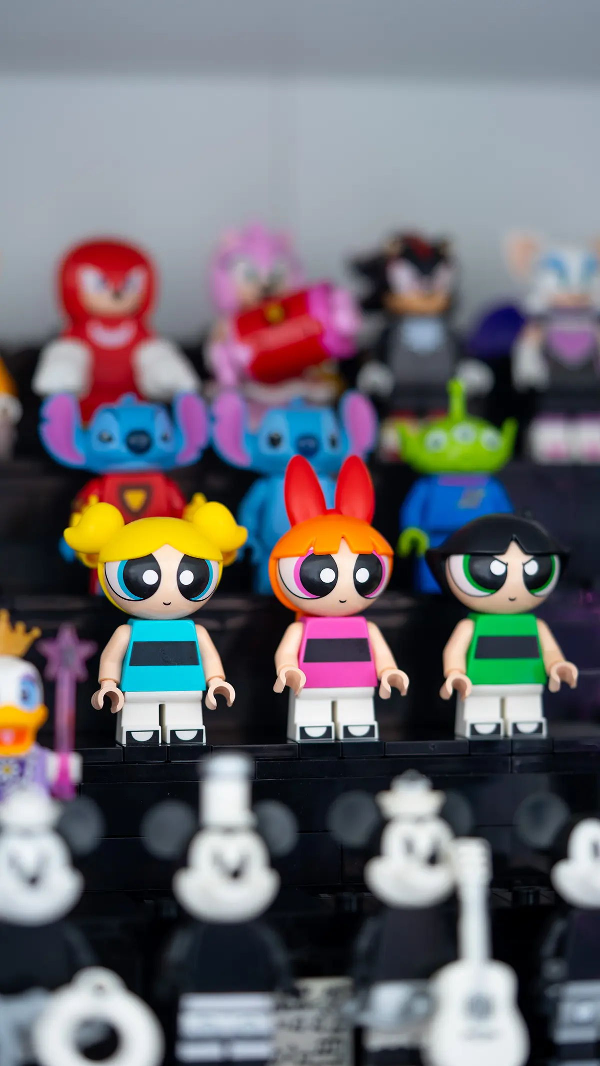 LEGO Powerpuff Girls minifigures—Bubbles, Blossom, and Buttercup—stand in front of characters from Disney and Sonic, including Stitch, Knuckles, and Mickey Mouse in black-and-white variants.