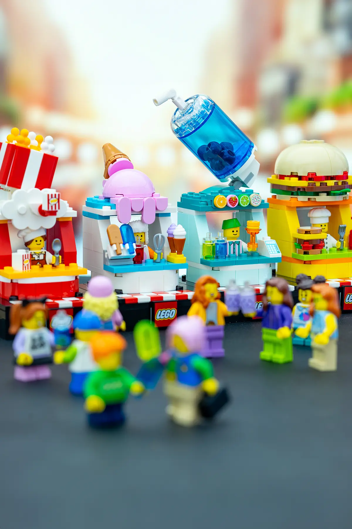 LEGO minifigures gather at a colorful street food festival featuring themed vendor stalls for popcorn, ice cream, drinks, and burgers, set against a bright city backdrop.