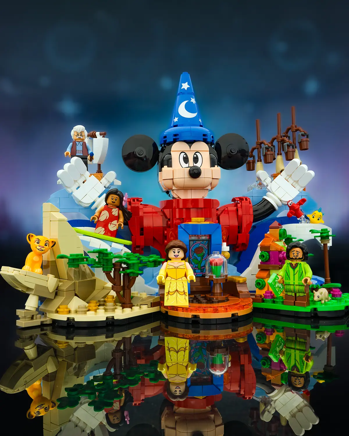 LEGO display featuring Sorcerer Mickey surrounded by Disney characters including Belle, Simba, Moana, and Mirabel, with themed scenery and a glowing magical backdrop.