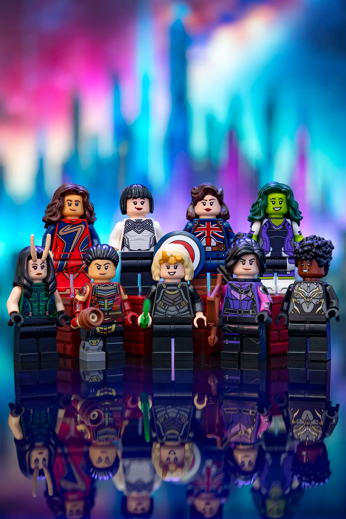 A vibrant group shot of LEGO Marvel female superheroes posed heroically against a glowing, colorful background. Featured characters include Scarlet Witch, Ms. Marvel, She-Hulk, Valkyrie, Captain Carter, Kate Bishop, Okoye, Mighty Thor, and others, reflecting strength, diversity, and unity in celebration of International Women’s Day. Their mirrored reflections add a dramatic and empowering touch to the scene.