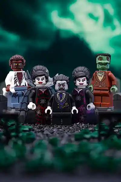A lineup of LEGO classic monsters—including Dracula, Frankenstein's monster, a werewolf, and two vampire brides—pose in a graveyard under an ominous green sky, exuding spooky Halloween vibes.