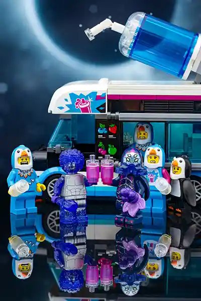 A fun LEGO scene with aliens and costumed minifigures enjoying vibrant pink slushies from a space-themed drink truck, set against a cosmic backdrop with stars and planets.